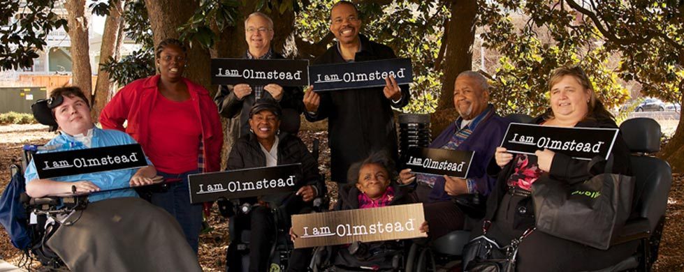 Diverse Group of People with Disabilities Holding I am Olmstead Signs