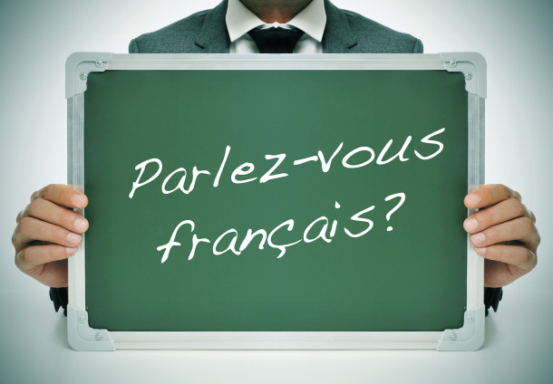 man wearing a suit holding a chalkboard with the question parlez-vous francais? do you speak french? written in it