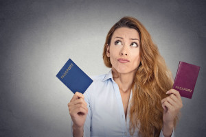 35166255 - portrait young woman holding two passports confused face expression isolated on grey wall background
