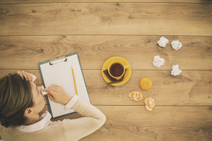 Sick woman blowing nose, sitting by the table, working at home office, drinking tea and eating citrus fruit while working. Directly above shot