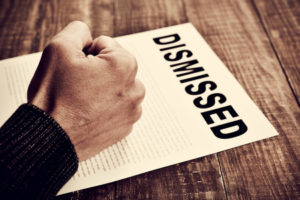52101162 - closeup of the fist of a young caucasian man on a document with the text dismissed, placed on a rustic wooden table