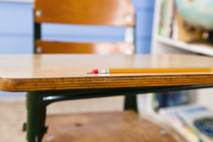 Pencil on student desk in a classroom with brick background