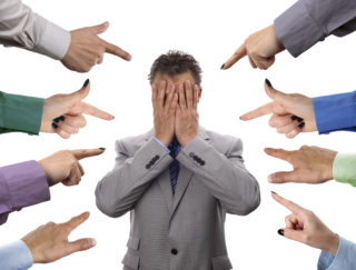 Hands pointing towards businessman holding head in hands concept for blame, accusations and bullying