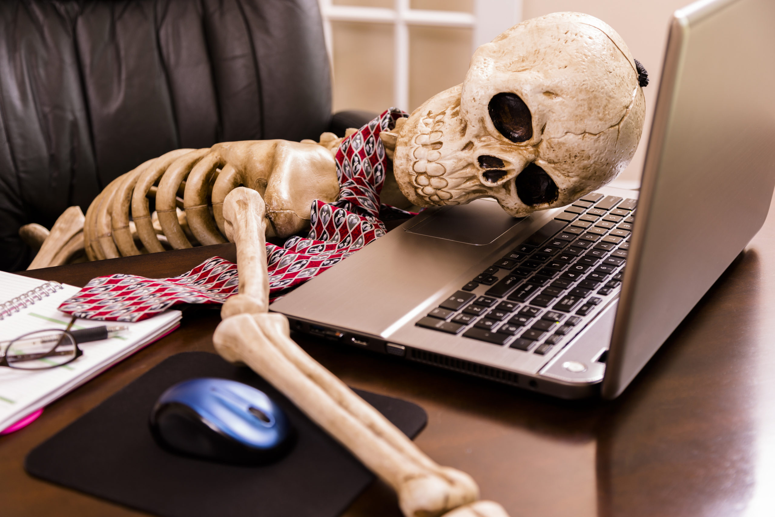 Working to death. Business man's skeleton using laptop in office.