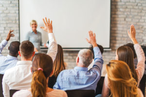 Rear view of business people with raised arms on seminar.