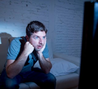 television addict man watching tv holding remote control mesmerized