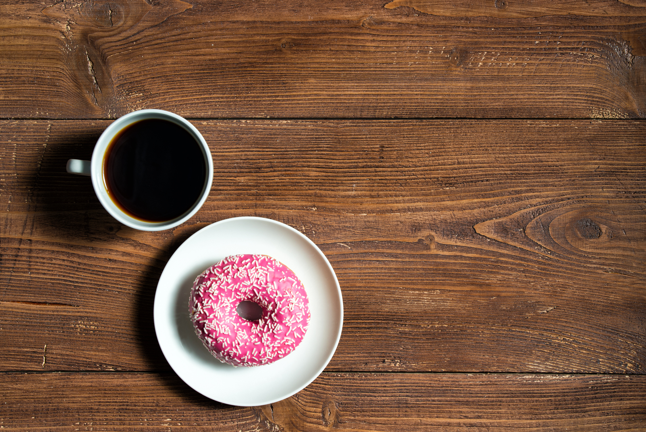 Cup of black coffee with pink donut on wooden background