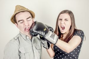 Photo of a woman jokingly punching a man in the face with boxing gloves on.