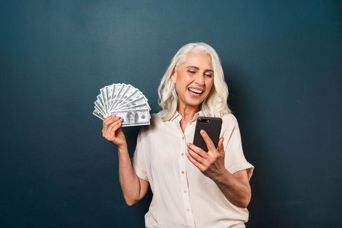 mature-happy-old-woman-holding-money-using-mobile-PHKS53Y.jpg
