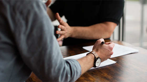 two men meeting, paperwork on a wooden table, perhaps a lender meeting for nonprofit organizations