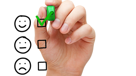 a woman's hand drawing a green check mark with a green marker next to a box with a smiley face, drawn above a medium smile face and sad face; image used for a blog post about getting feedback for not-for-profits