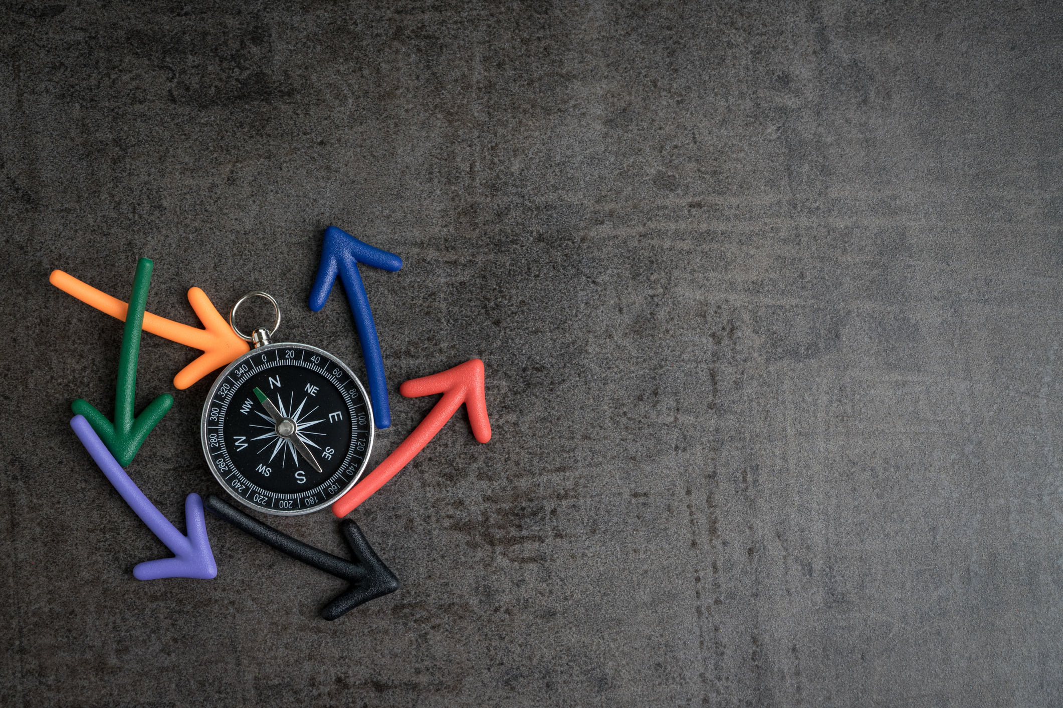 Uncertain path or multiple random life fortune and directions concept, compass at the center with magnet arrows pointing random multi directions on dark black chalkboard cement wall with copy space