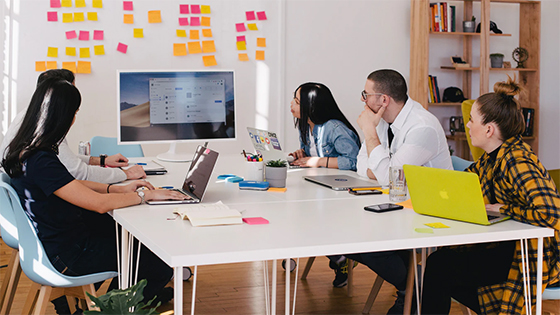 five people sitting around a table looking a board of multi-colored sticky notes; image used for blog post about real-time strategic planning for not-for-profits