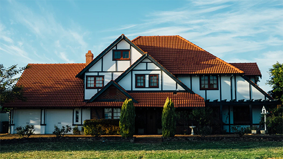a photograph of a white paint house with copper orange roof, with green grass lawn and a cloudless blue sky; image used for a blog post about homes providing a tax break