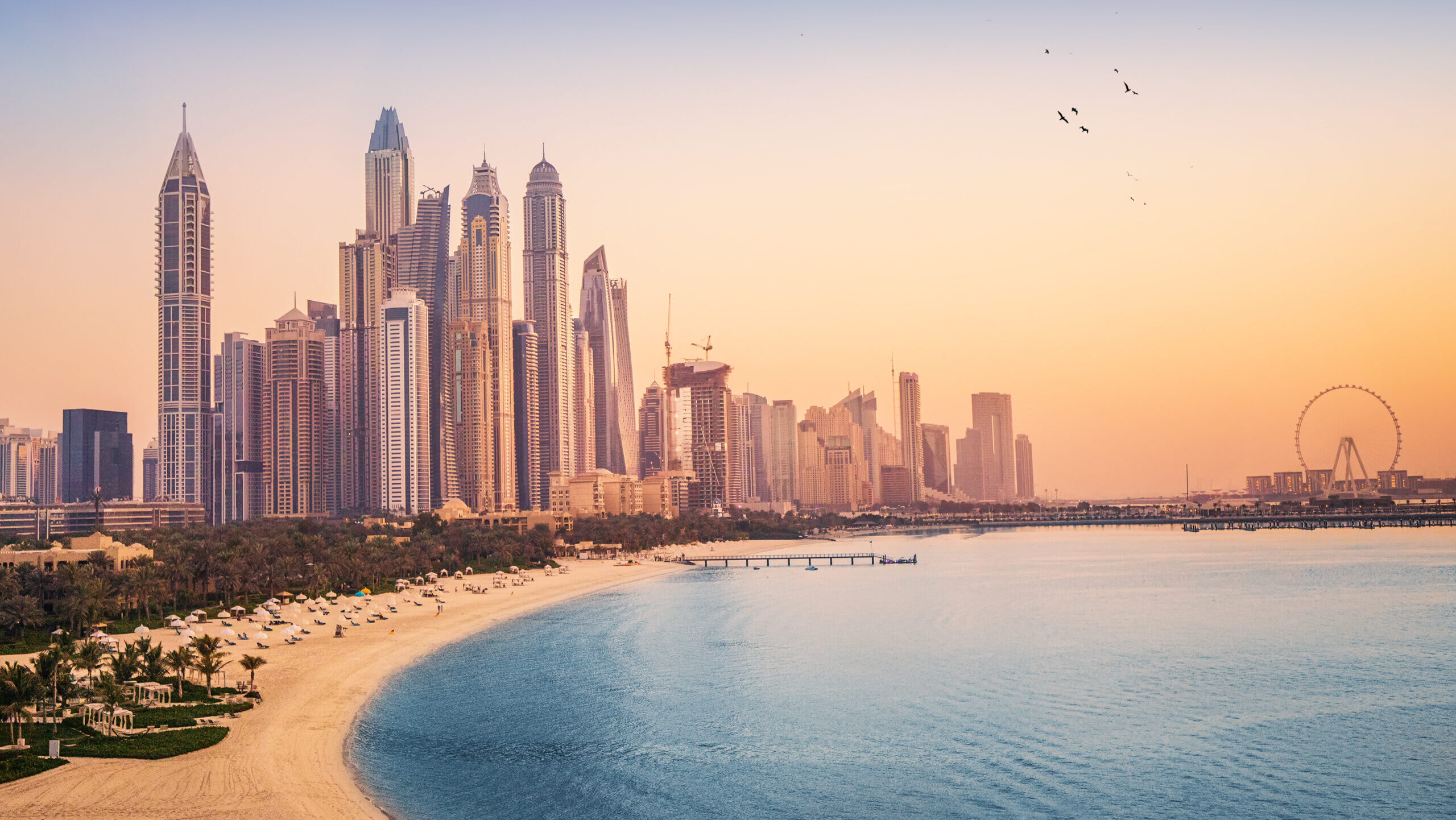 Sunset view of the Dubai Marina and JBR area and the famous Ferris Wheel and golden sand beaches in the Persian Gulf. Holidays and vacations in the UAE