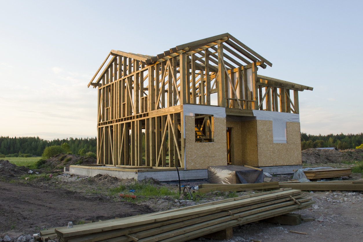 Skeleton of a wooden two-story cottage surrounded by building materials