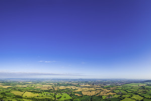 Big blue summer skies over picturesque patchwork landscape of green pasture and golden crop fields, rural villages, farms and country towns. ProPhoto RGB profile for maximum color fidelity and gamut.
