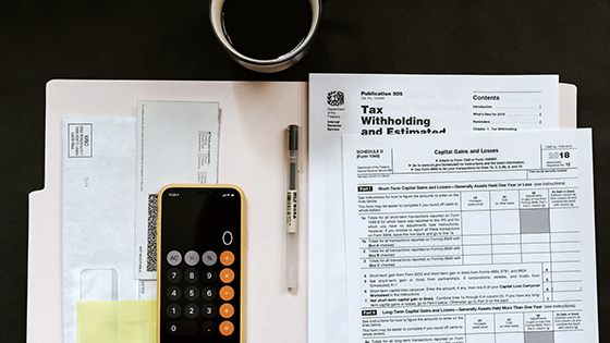 tax filing documents sitting on top of a manila folder with envelopes, a sticky note and a cell phone showing a calculator; image used for blog post about considerations for July 15 2020 tax filing deadline during COVID-19 pandemic