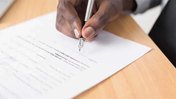 man holding a pen to paper about to sign a contract; image used for a blog post Main Street Lending Program during COVID-19 pandemic
