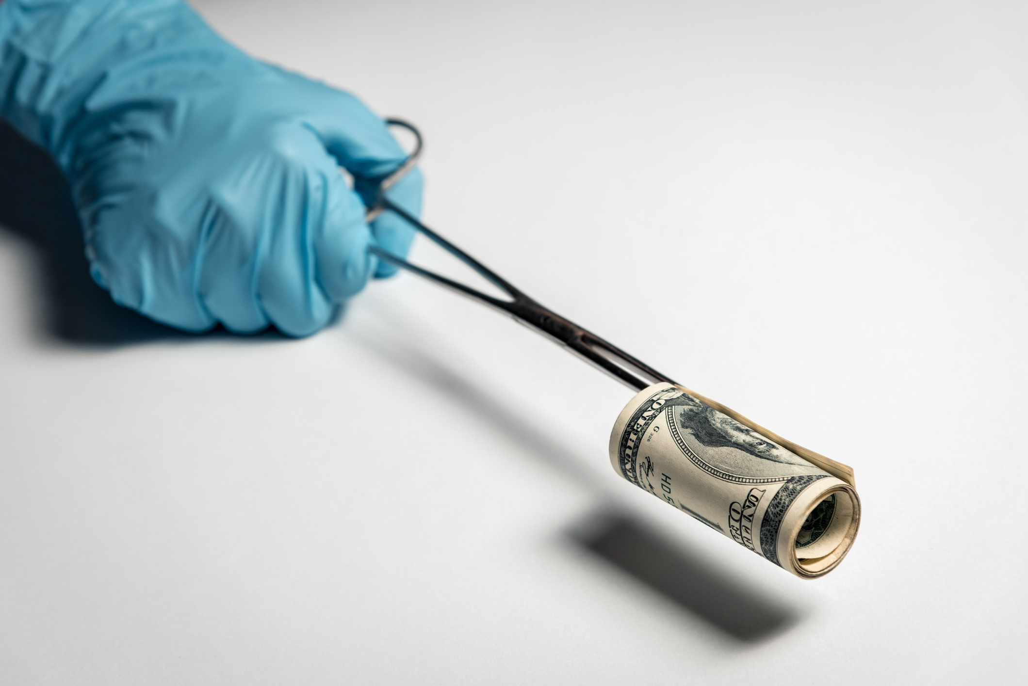 Doctor's hand holds a bundle of dollars with the help of medical forceps. Bribe to the doctor, buying remedies against coronavirus. Horizontal frame