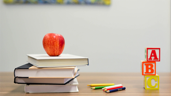 an apple sitting on top of a stack of books next to colored pencils and A-B-C blocks; image used for blog post about educational tax breaks