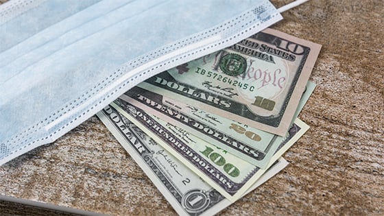 dollar bills sitting underneath a medical mask; image used for blog post about deferral of employees' social security tax
