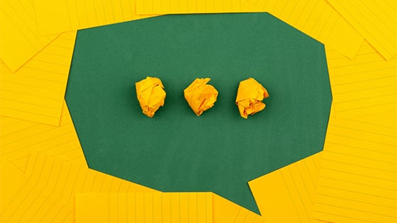 green and yellow paper forming a speech bubble with an ellipses; image used for blog post about easing not-for-profit staffers' anxiety