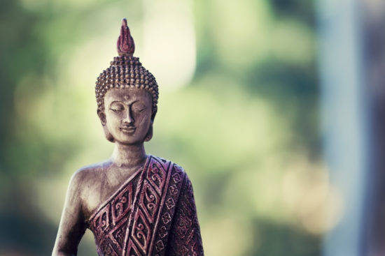 Buddha statue isolated outside on nature and green background with copy space. Buddhism symbol of religion, peace and spirituality