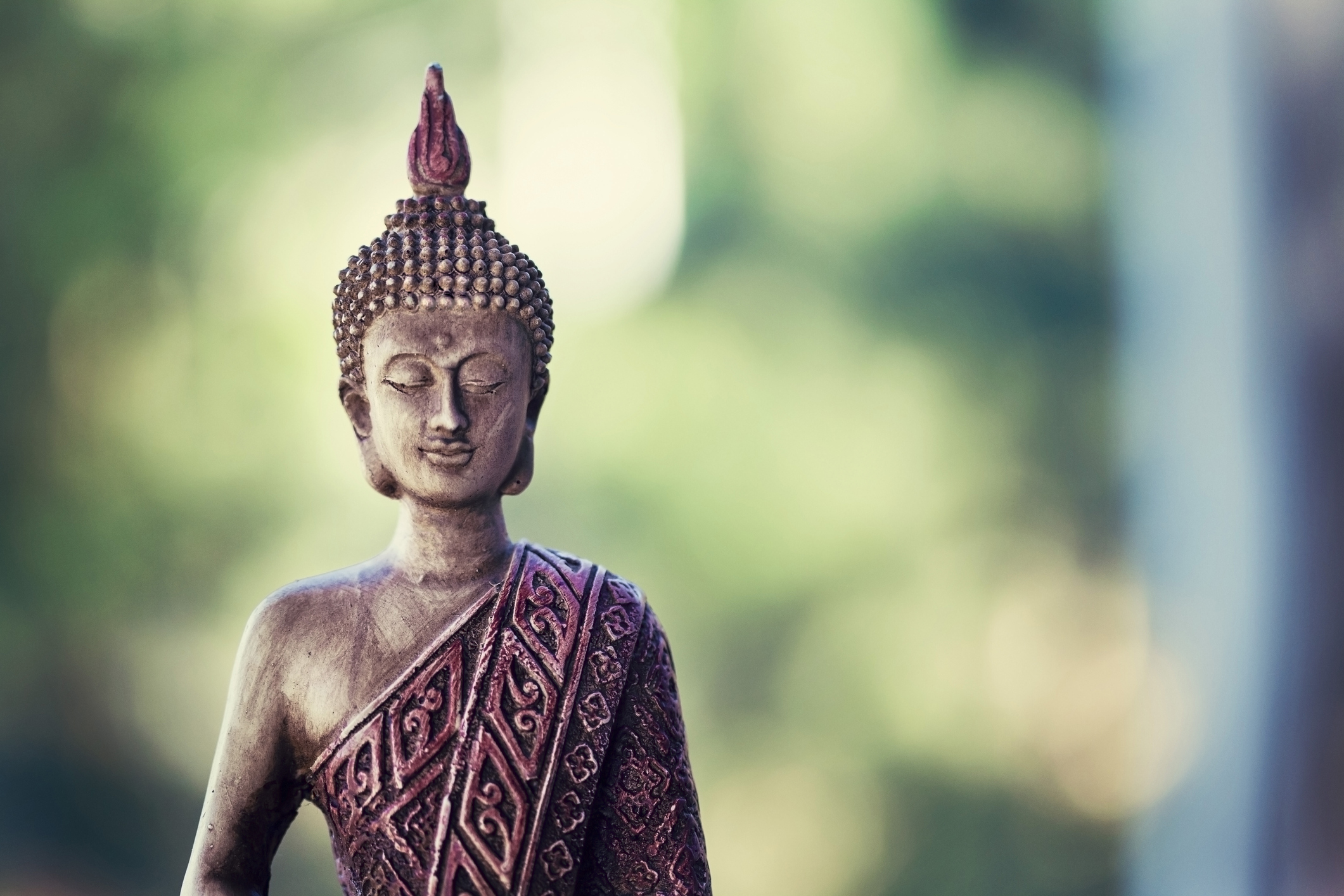 Buddha statue isolated outside on nature and green background with copy space. Buddhism symbol of religion, peace and spirituality
