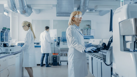 Team of Research Scientists Working On Computer, with Medical Equipment, Analyzing Blood and Genetic Material Samples with Special Machines in the Modern Laboratory.