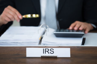 Midsection of tax auditor examining documents with magnifying glass at table in office