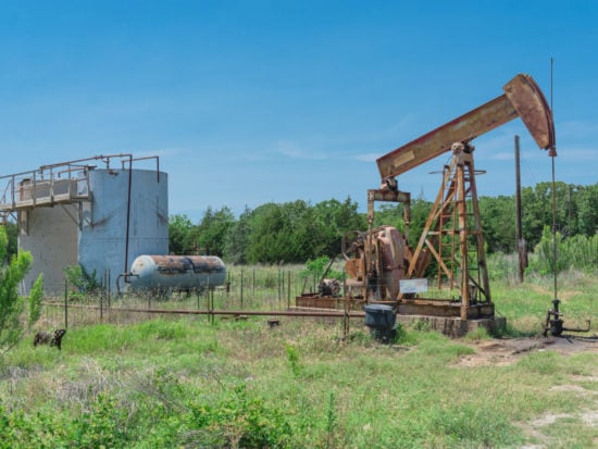 Rustic working pump jack pumping crude oil out of well to tank. Pumper and water emulsion at oil drilling site in Gainesville, Texas, US. Old pump jack, oil tanks for Energy and Industrial background