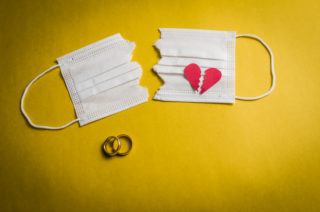 Great concept of divorce in quarantine due to the 2019 coronavirus pandemic. Face mask cut in half with wedding rings.