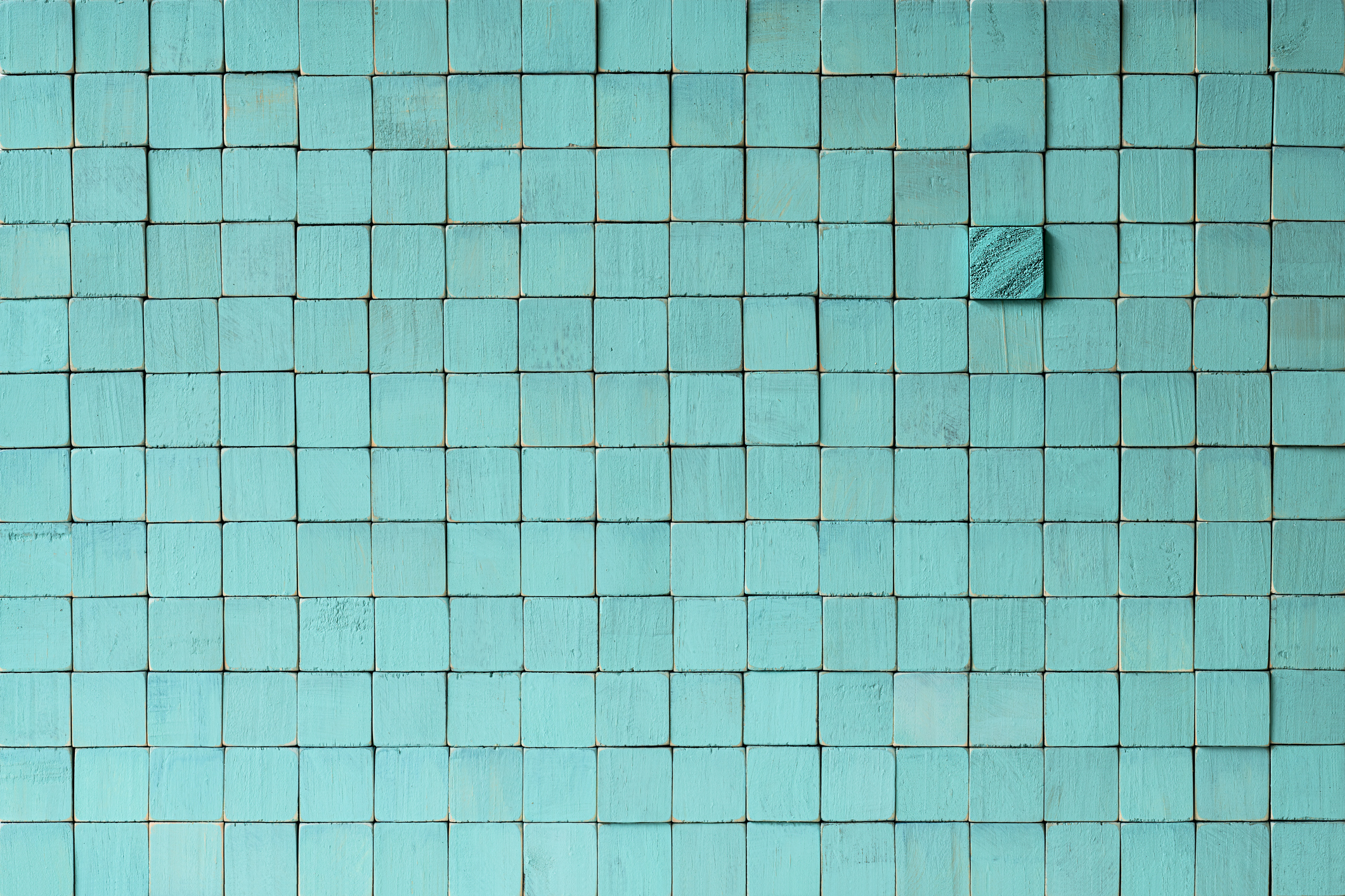 Many square wood textured colorful turquoise colored wooden blocks stacked up on top of each other with one different grain block standing out from the crowd in contrast to the others, creating a wood grained abstract background.
