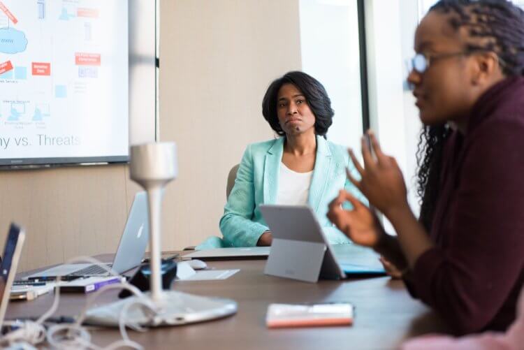 Legal Project Manager in Meeting A woman in a business suit listens to another woman, a legal project manager, explain a project
