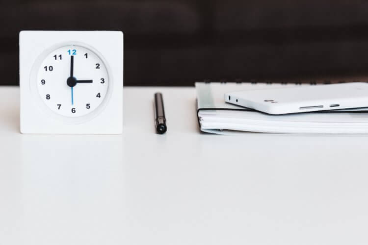 A small clock sits next to a pen and a notepad, all neatly organized on a legal project manager's white desk