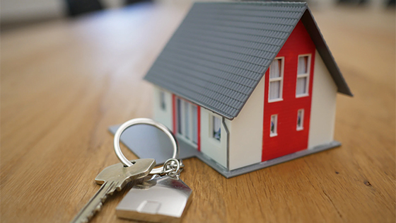 white and red wooden house miniature on brown table with a silver key; image used for blog post about planning your estate or inherited assets and property