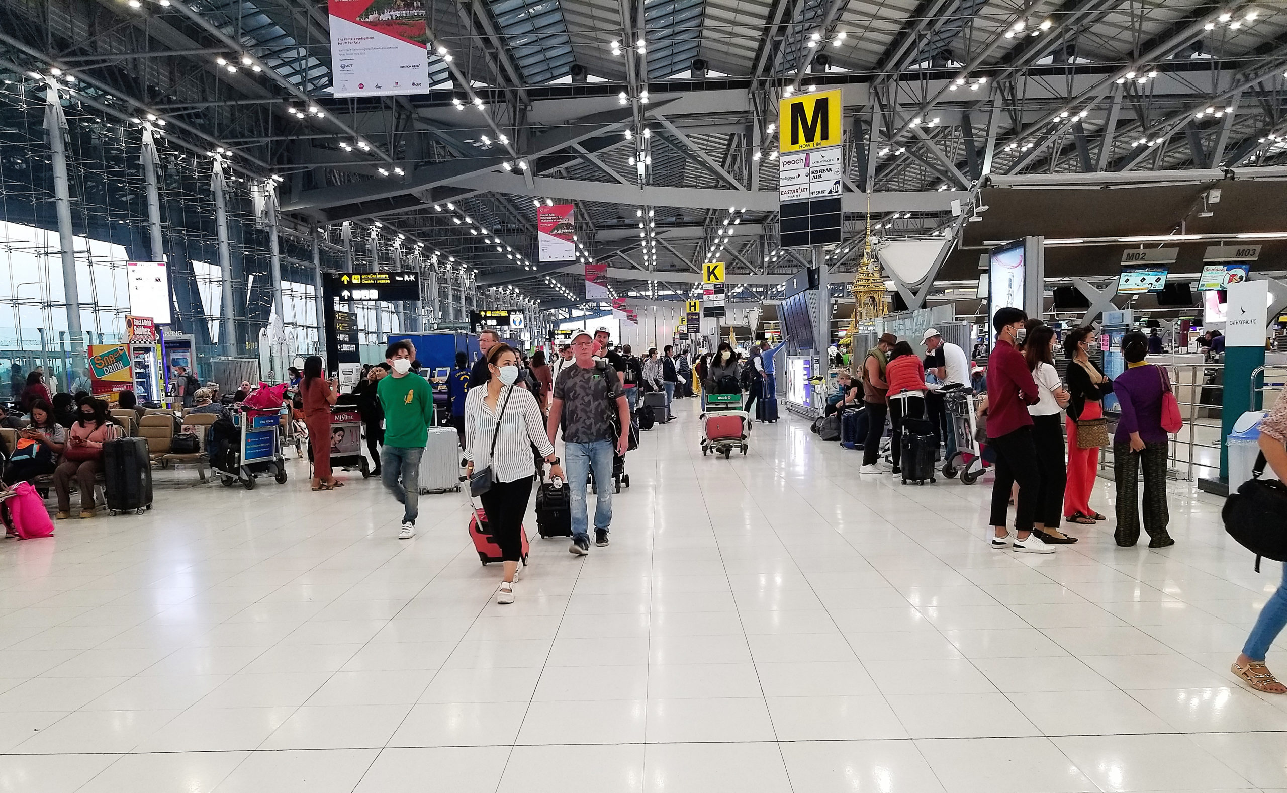 Travelers with luggage at the airport in Bangkok wearing masks for protection against the Coronavirus