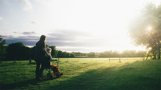 a person pushing an elderly person in a wheel chair across grass and sunset; image used for blog post about tax aspects for putting parent into a nursing home