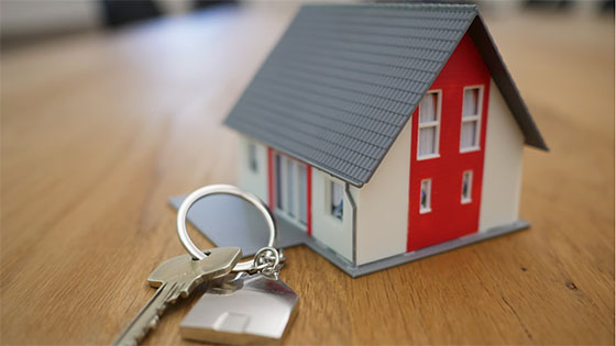 a small home figure sitting on a wooden desk with keys; image used for blog post about owing tax when selling a home