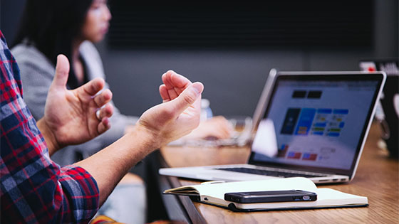 a person sitting at a table looking at a laptop and talking with their hands to someone; image used for blog post about not-for-profit restructuring