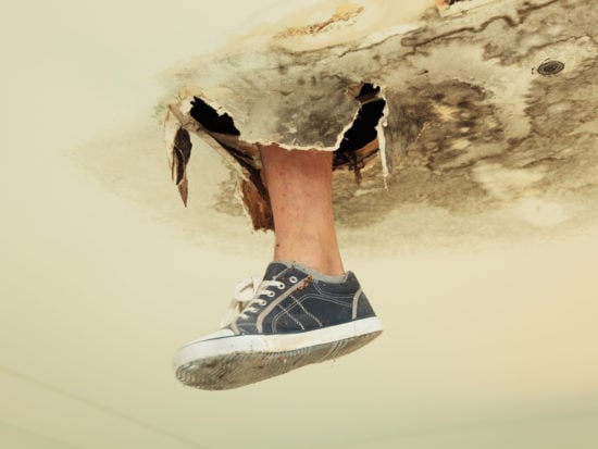Foot in canvas shoe poking through rot in the ceiling