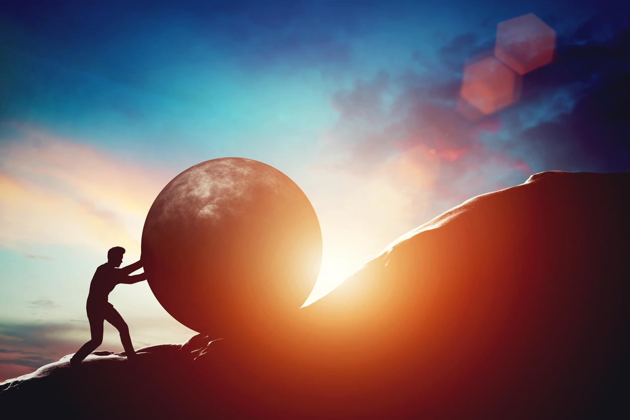 Man pushing huge concrete ball up hill.