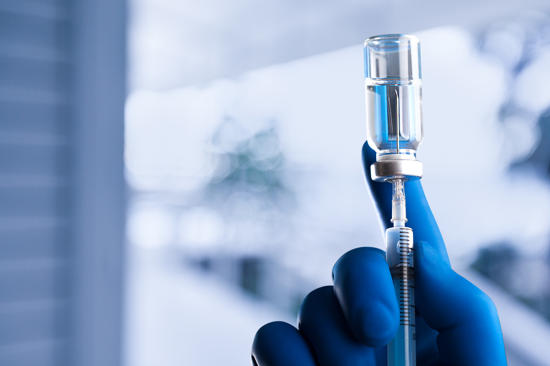 A medical hand in a glove holds an ampoule with a vaccine and a syringe with illustration