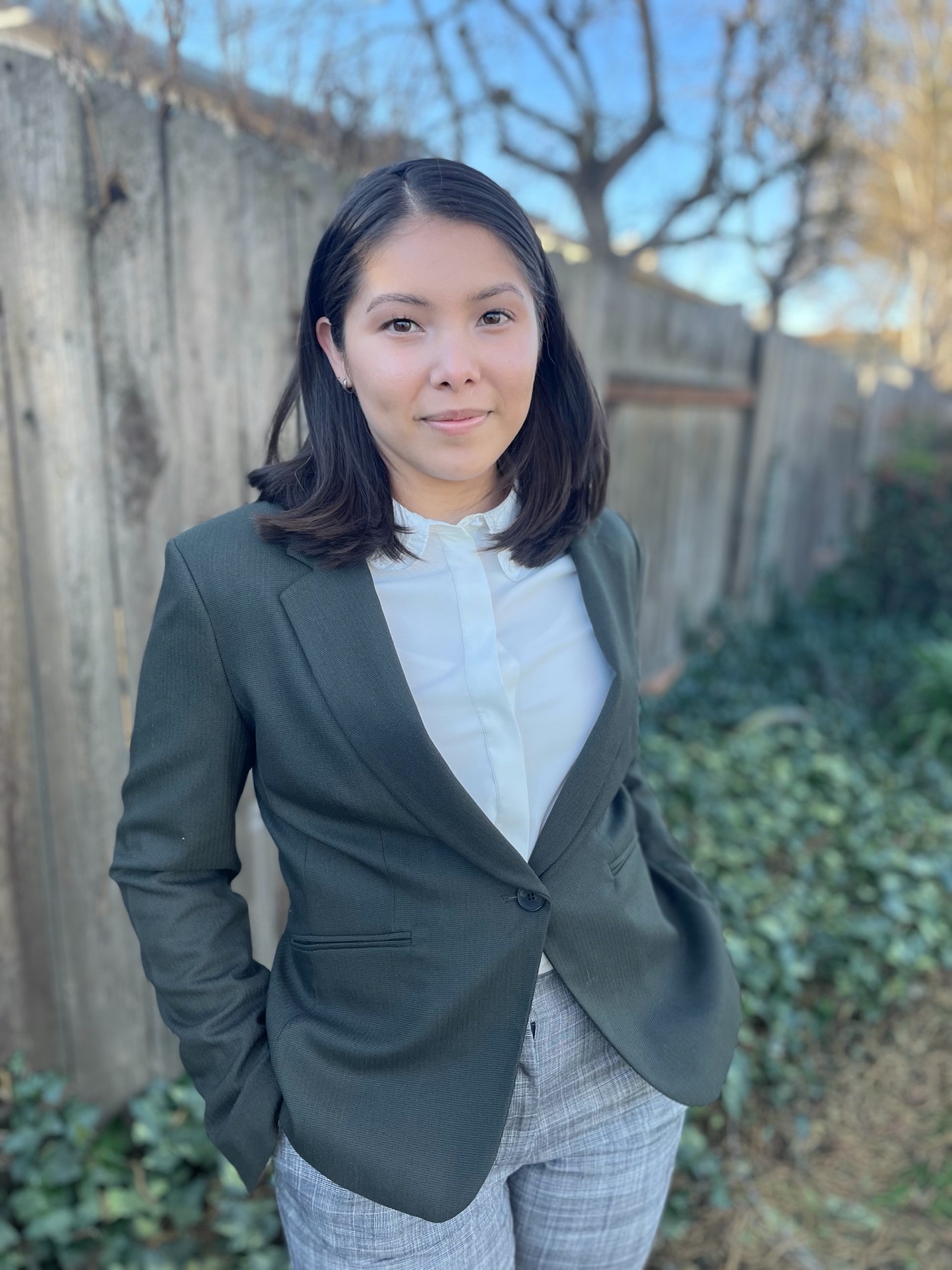 A woman in a suit poses near a fence