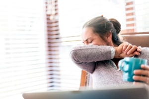 Woman coughing into arm representing covid-19 workplace claims