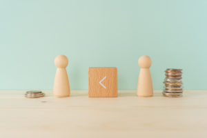 two wooden figures alongside unequal piles of coins showing inequality for pay for national pay day