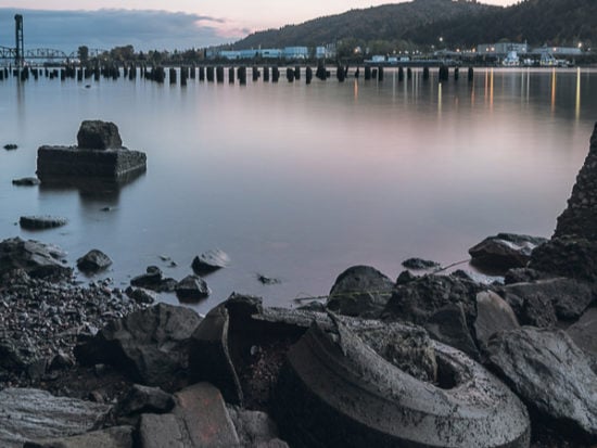 The rocky bank of the Willamette River near St. John's. The train bridge is in the distance and an old tire blends in with the rocks Superfund cleanup