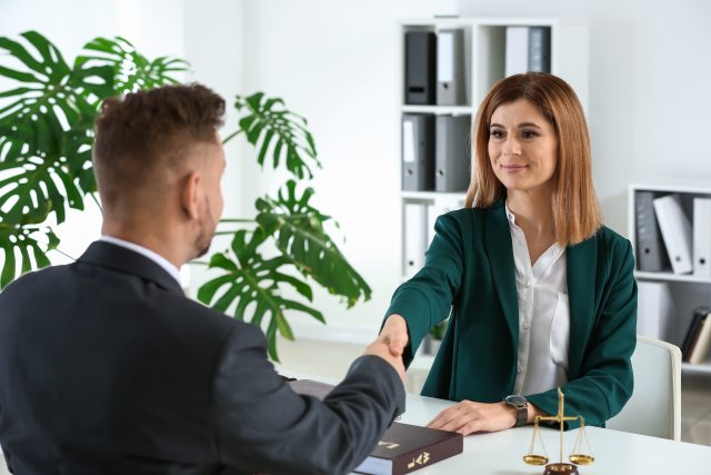 Woman shaking hands with an attorney across the table looking satisfied. Clement Law.