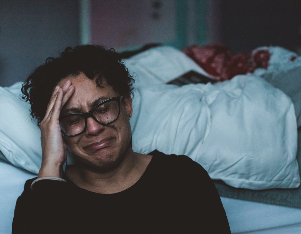 Woman sitting beside bed crying.
